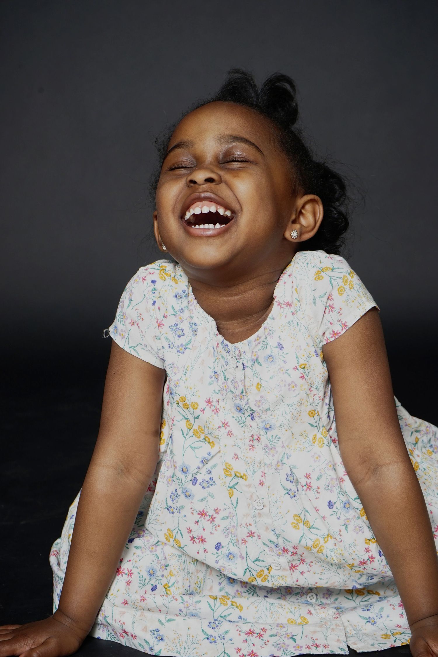 A joyful young Black girl in a floral dress laughs with eyes closed against a dark background.