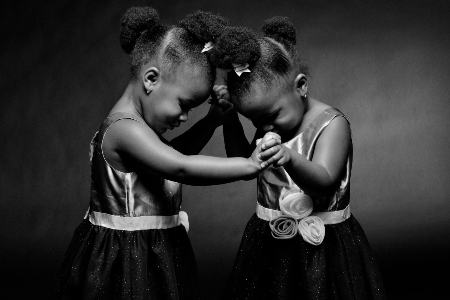 Black and white portrait of two young girls in matching dresses holding hands together.
