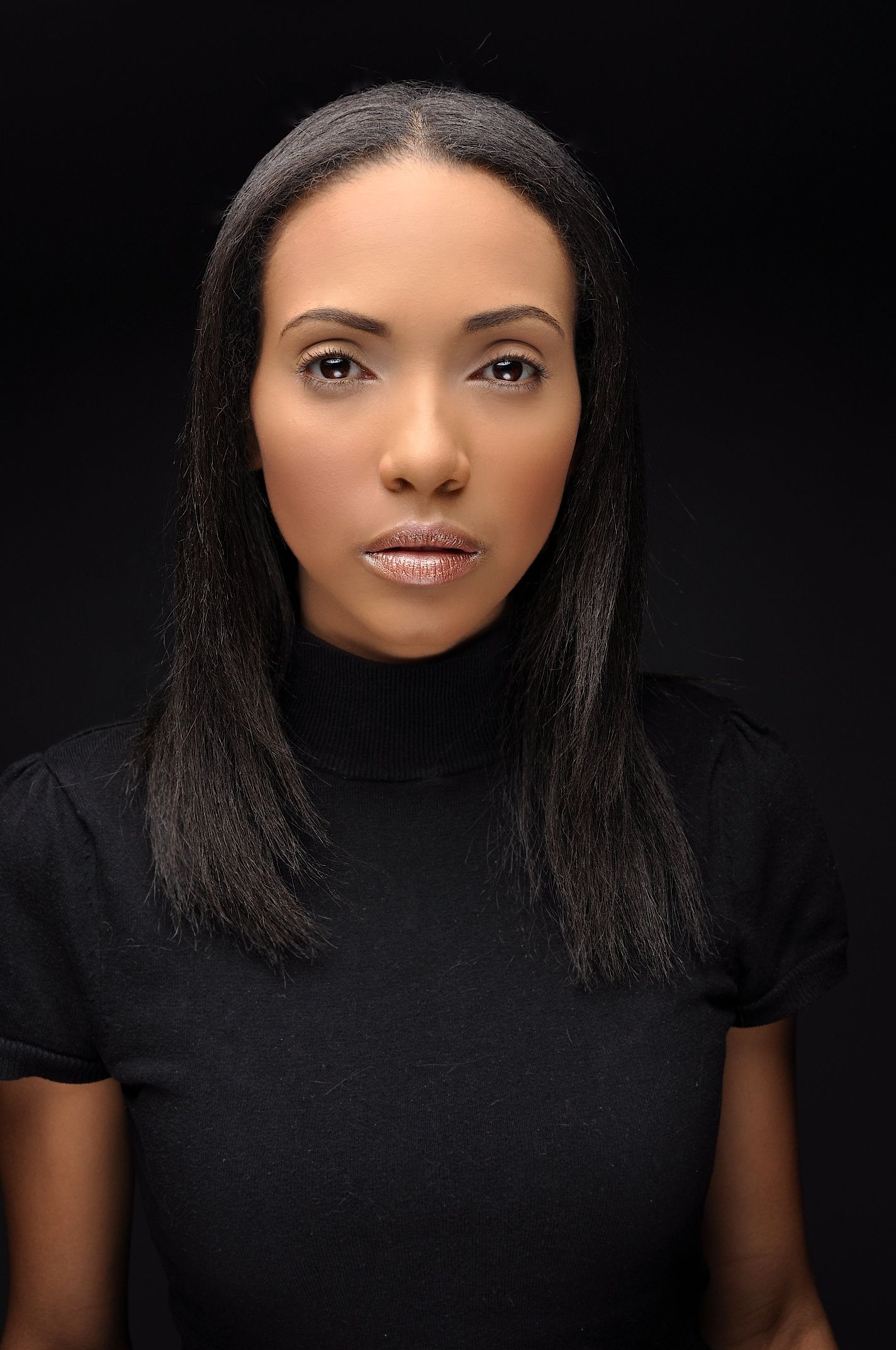 Professional portrait of a young Black woman with straight black hair wearing a black turtleneck top against dark background.