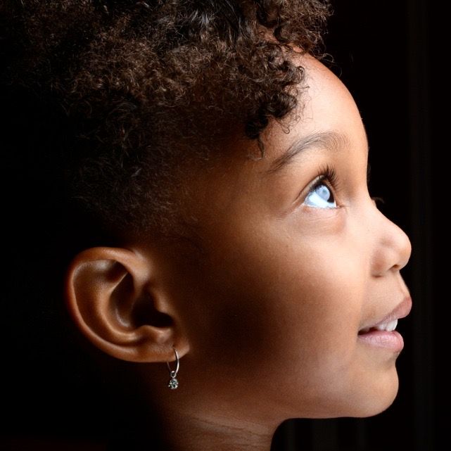 Close-up profile portrait of a young Black girl with curly hair and small earring looking upward.