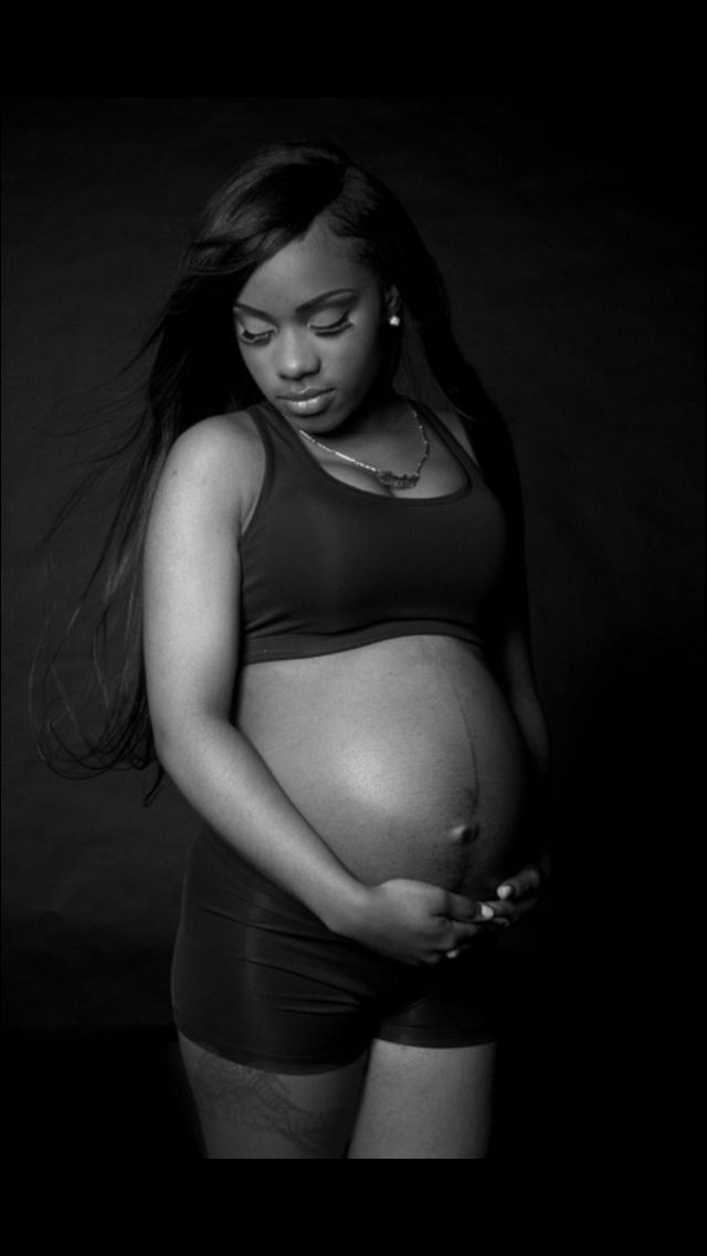 Black and white maternity photo of a pregnant woman cradling her baby bump in a dark studio setting.
