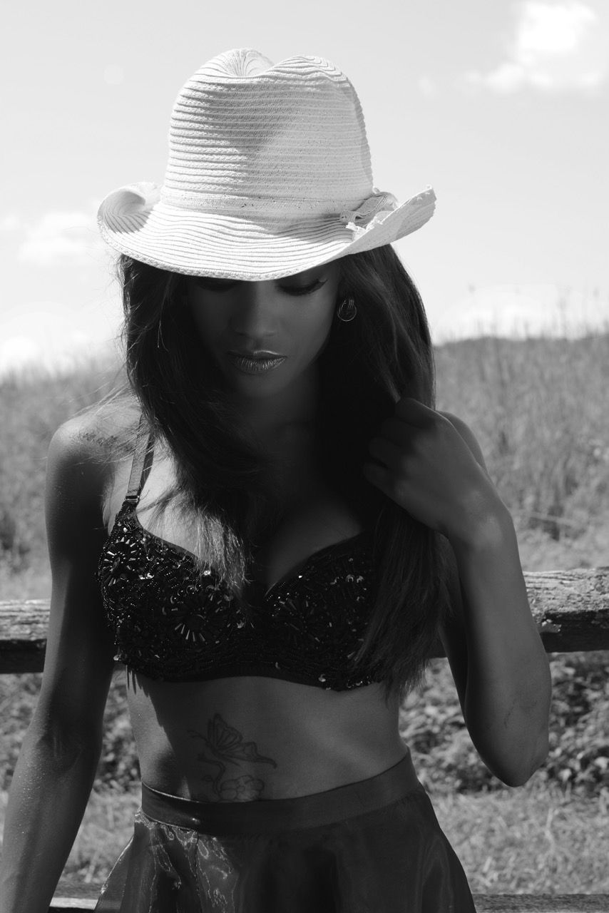 Black and white photo of woman in bikini top and cowboy hat posing outdoors.