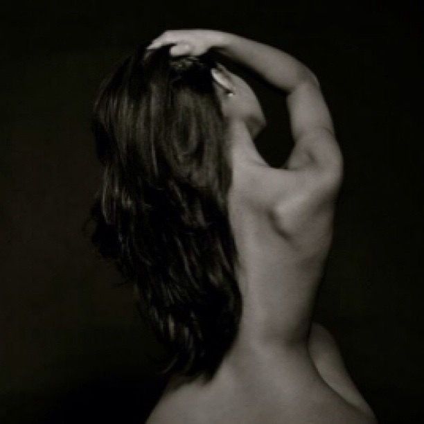 A black and white artistic portrait of a woman seen from behind with flowing dark hair raised overhead.