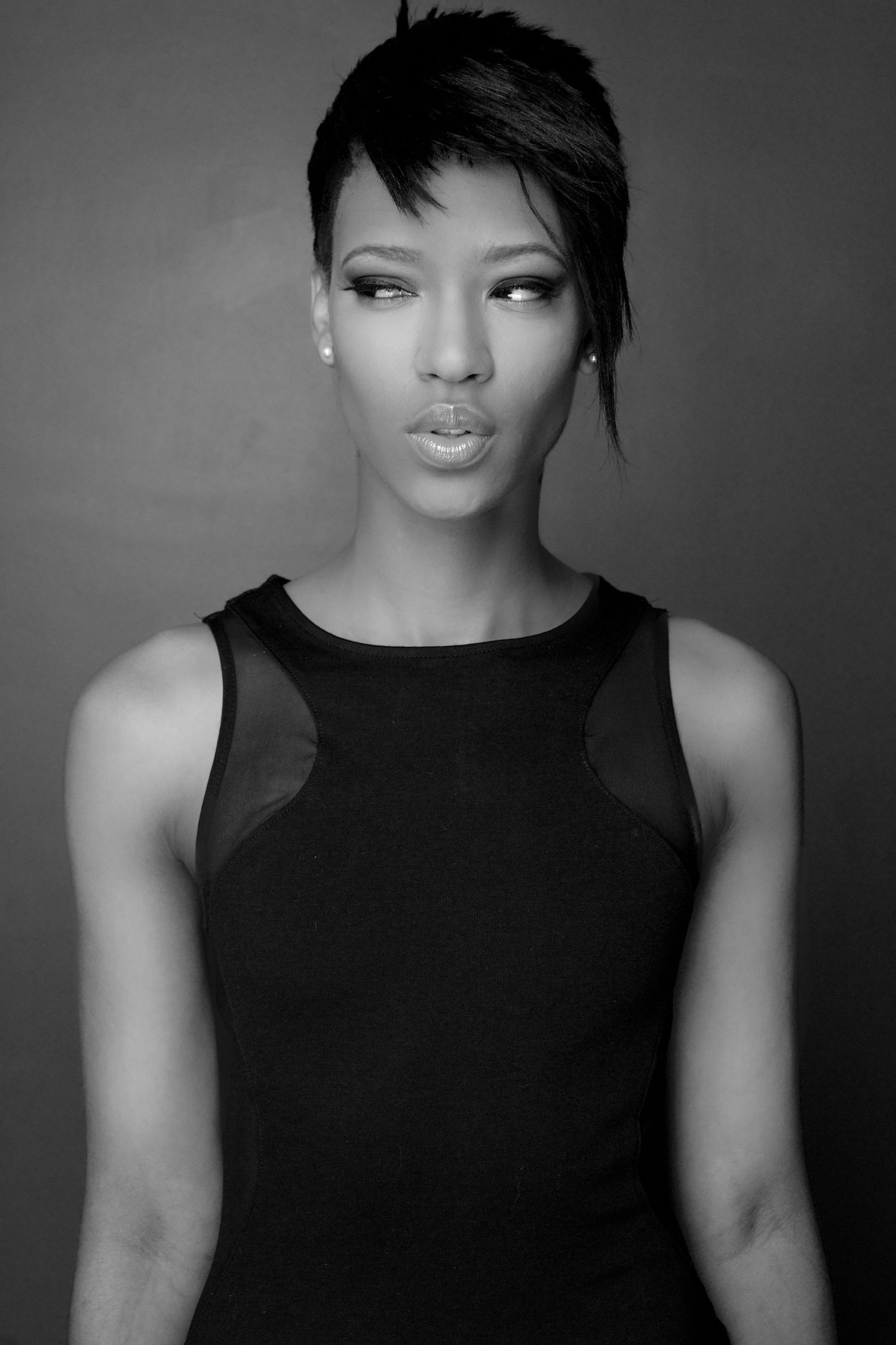Black and white portrait of a slender Black woman in black dress with short asymmetric haircut.