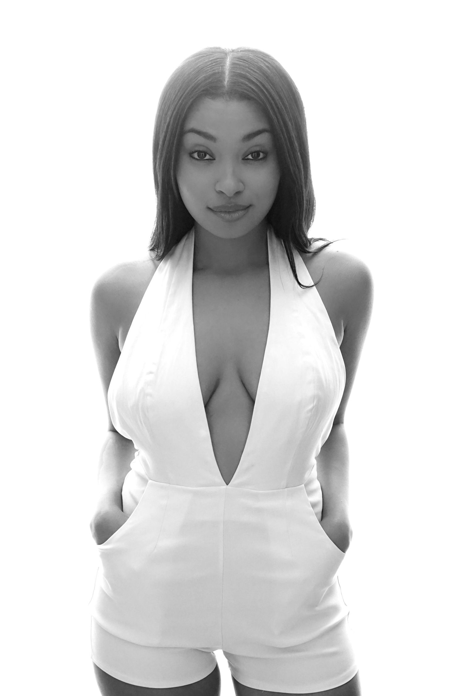 Black and white portrait of a woman in a white deep-V halter romper posing on white background.