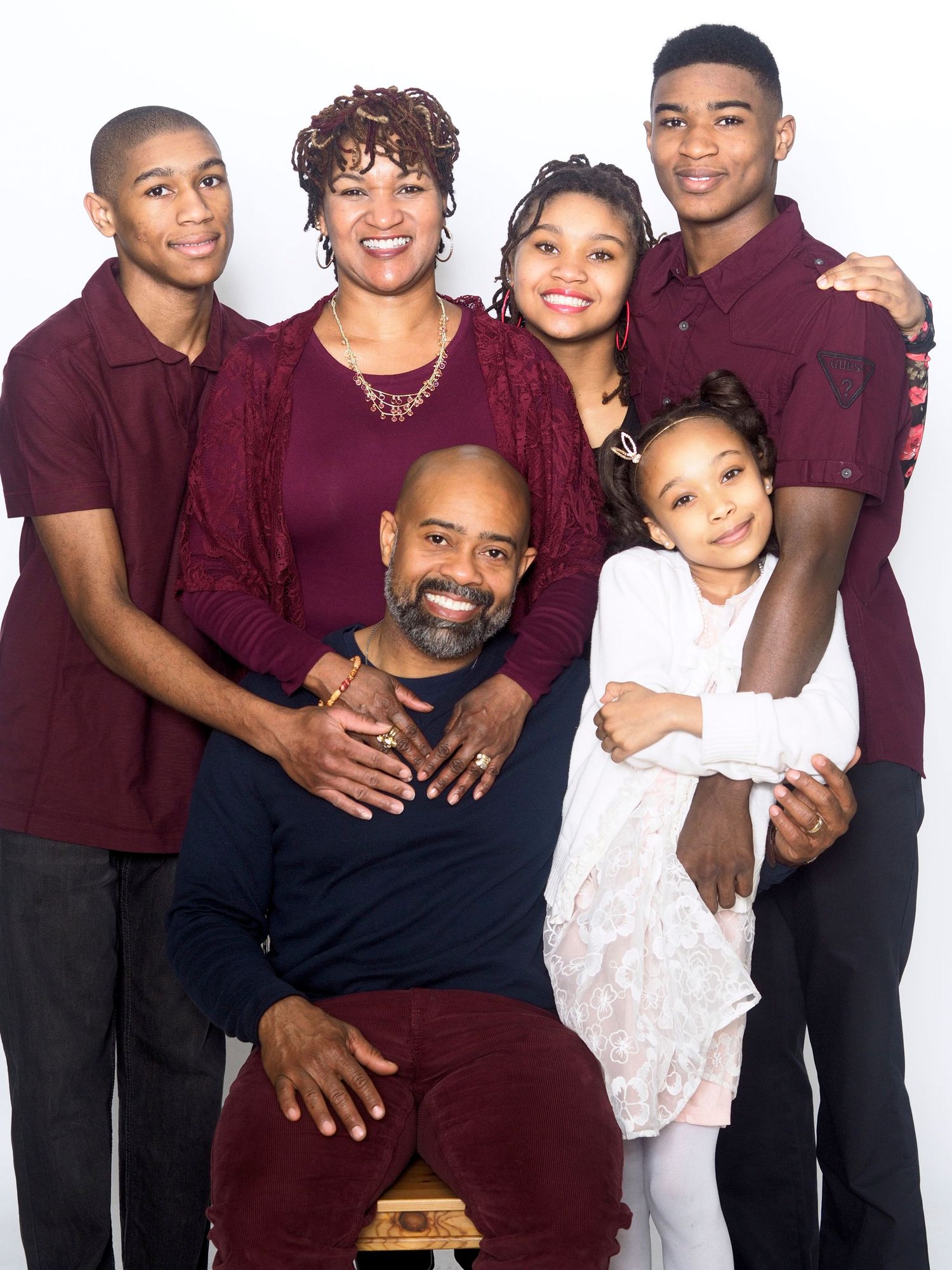 A happy Black family of six in coordinating burgundy and navy outfits poses together for a portrait.