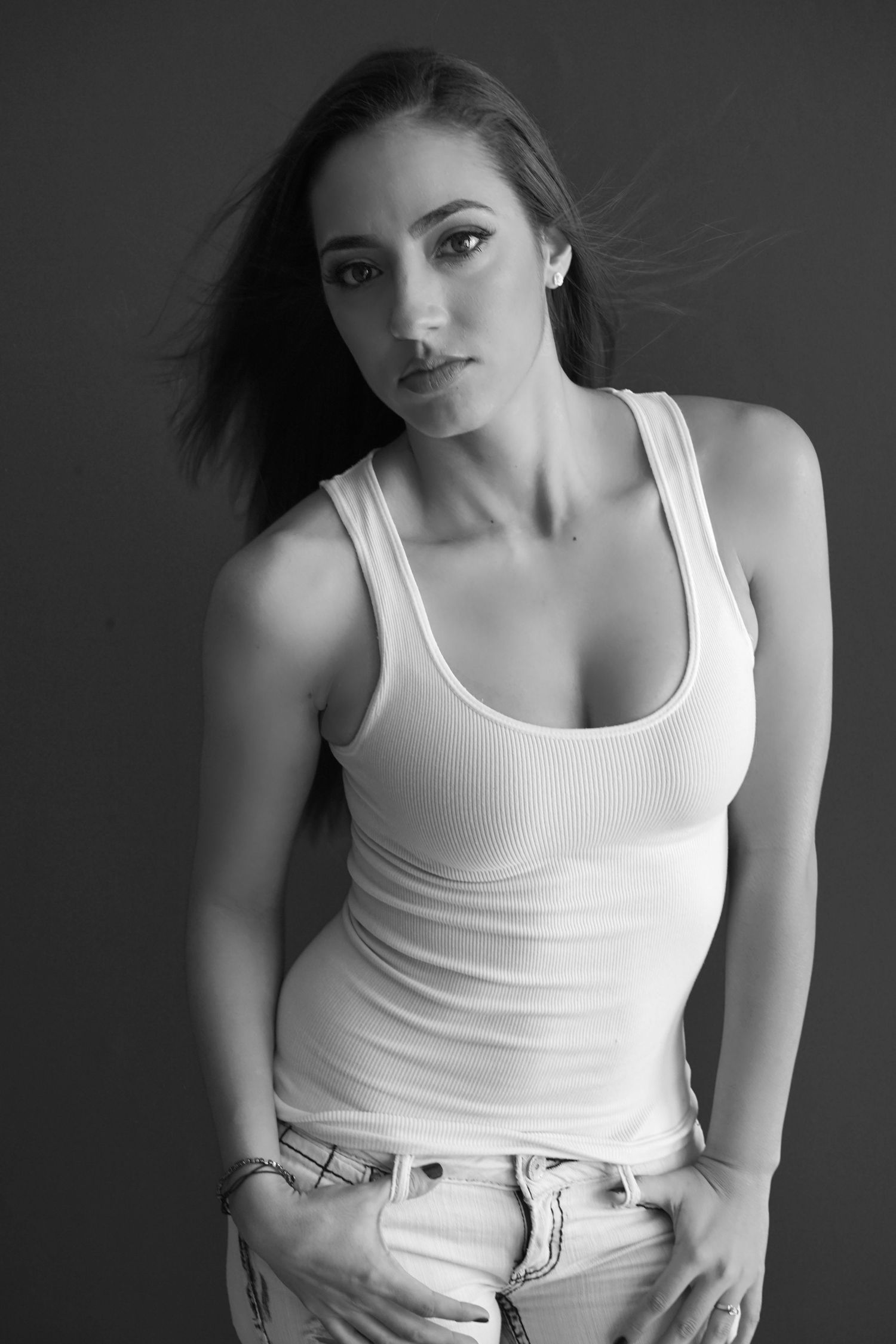 Black and white portrait of a young woman in a white tank top and jeans posing confidently.