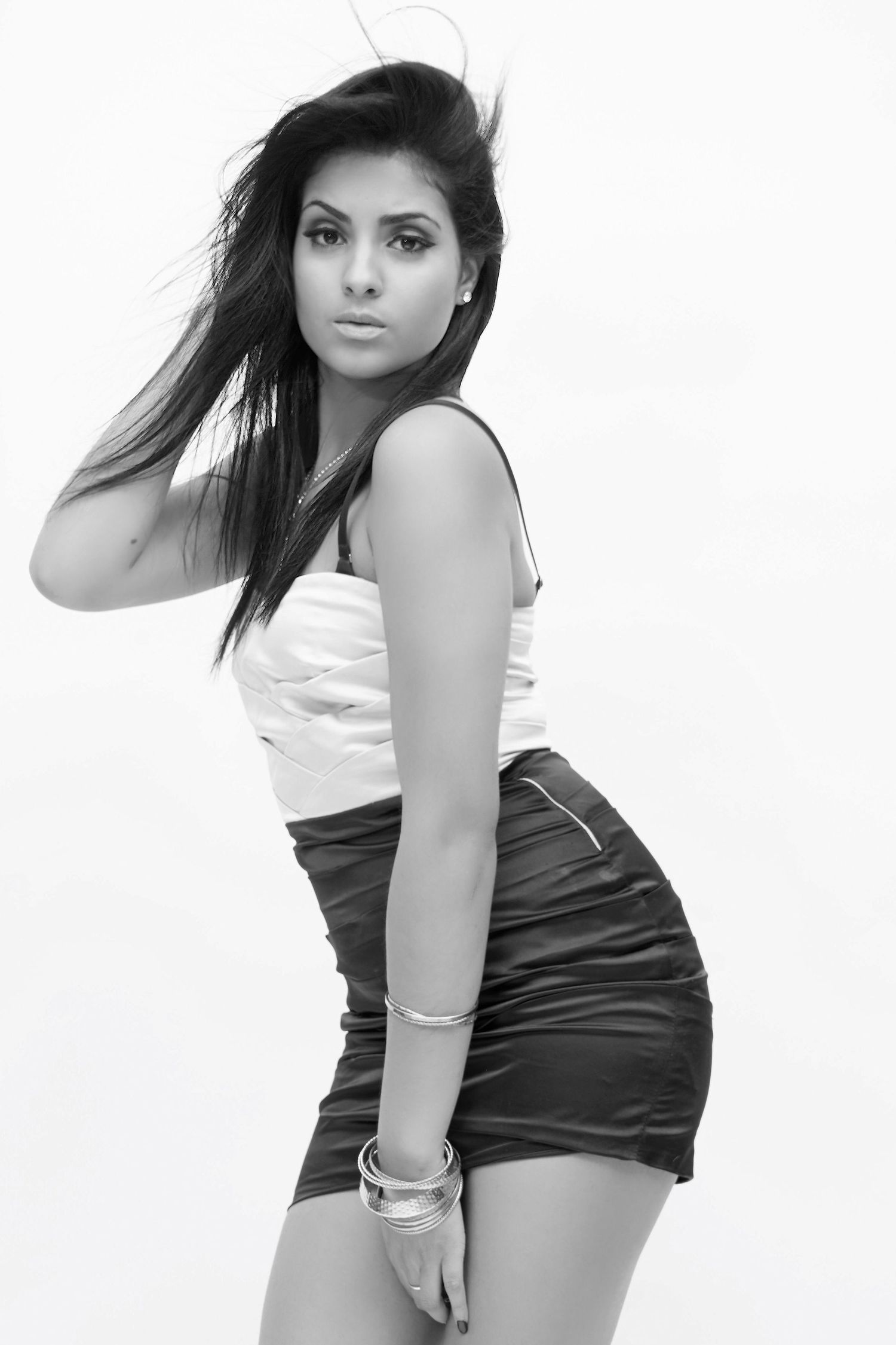Black and white photo of a young woman in a white top and black mini skirt with wind-blown hair.