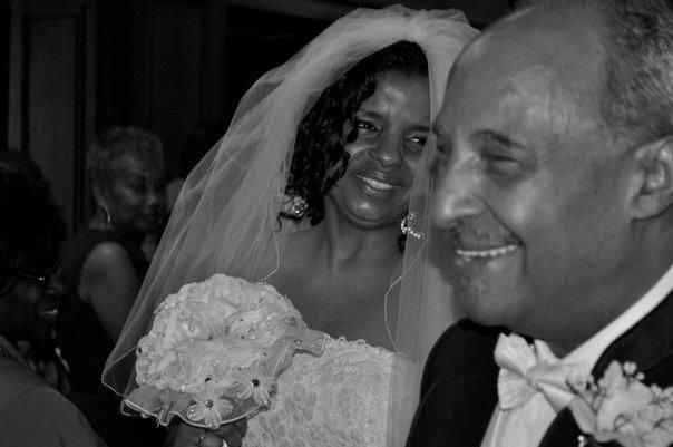 Black and white candid photo of a smiling bride holding bouquet with groom at wedding ceremony.