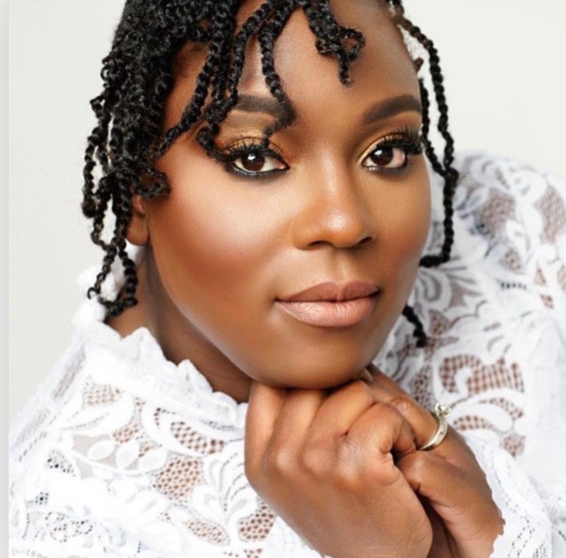 Woman with braided hair in white lace top posing with hands clasped together.