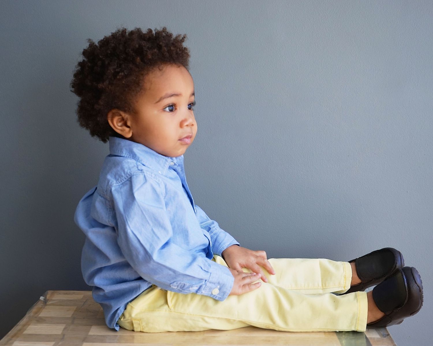 Toddler boy in blue shirt and yellow pants sitting on a checkered surface.