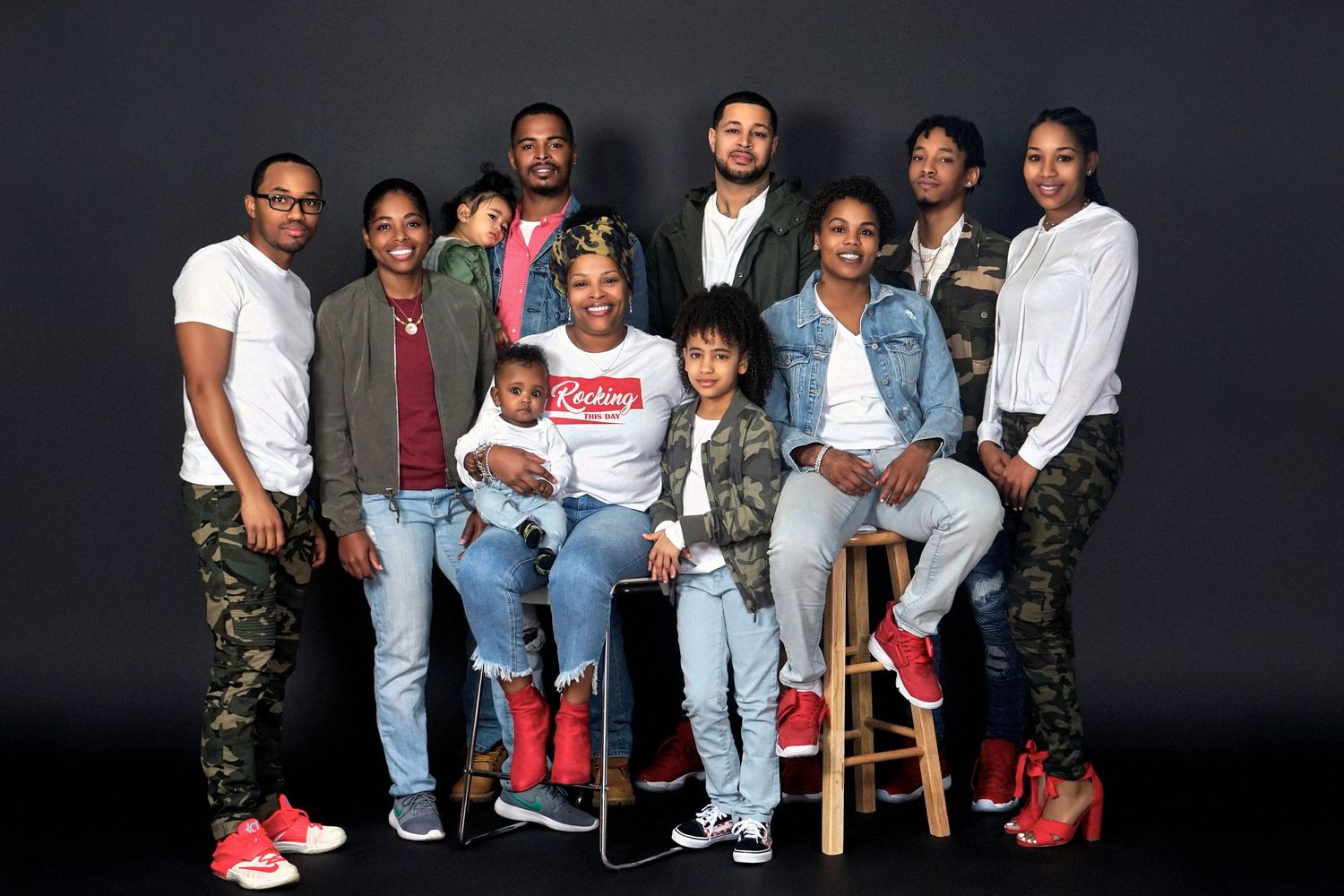 A diverse family group of ten people poses together for a professional portrait against a dark gray background.