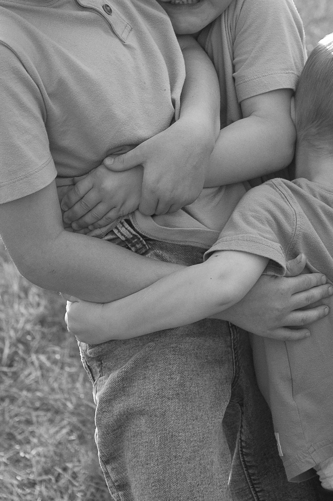 Black and white close up of three brothers in bare hug, documentary style photograph, candid real moments.