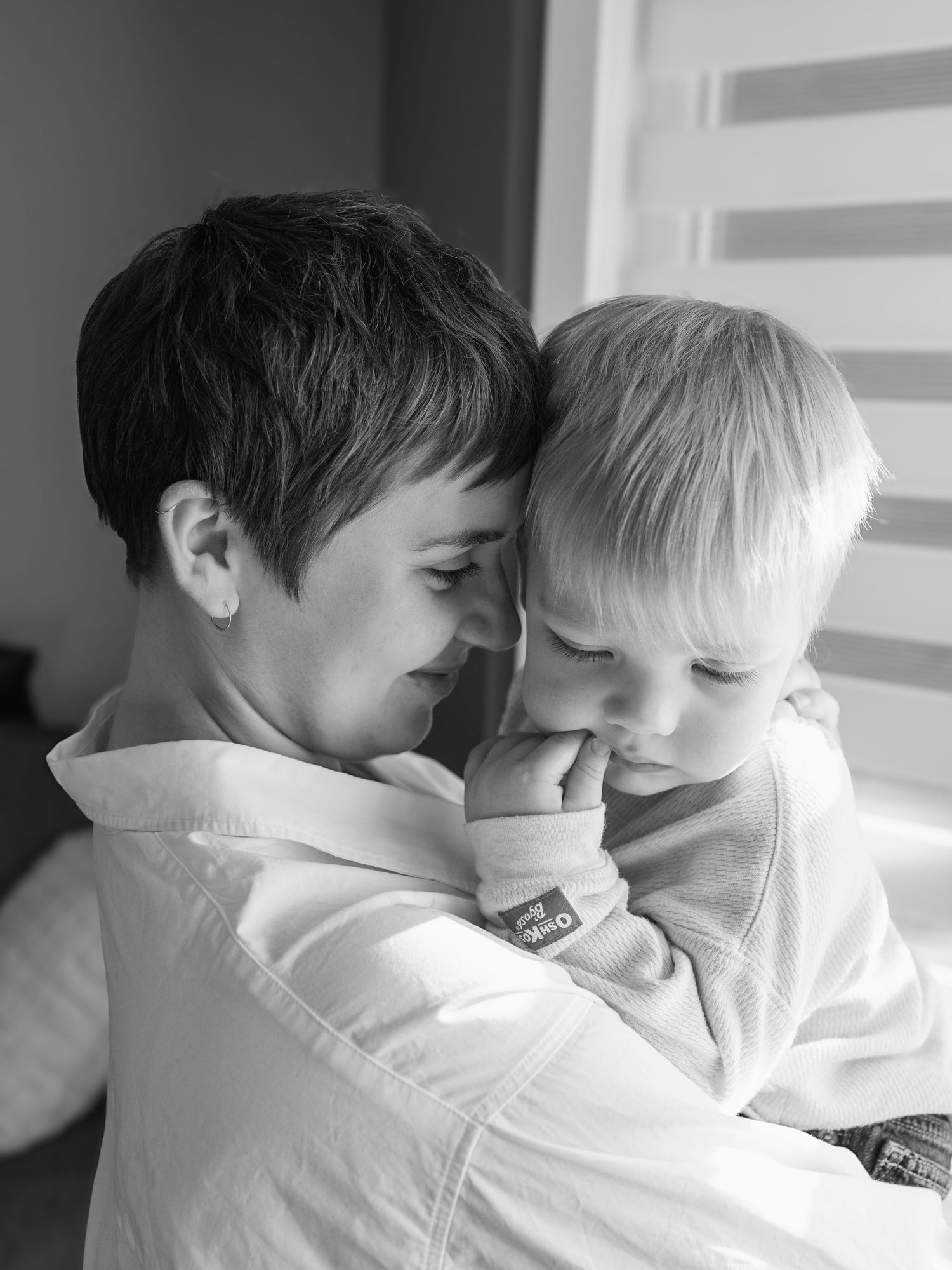 Black and white image of mother holding toddle and touching heads, smiling
