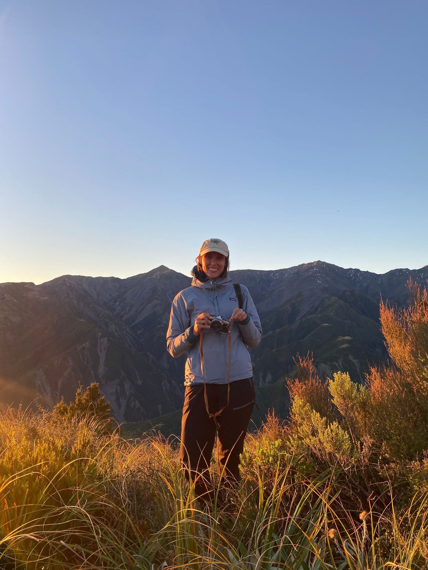 Colour image of woman in the mountains at sunset, smiling and holding film camera