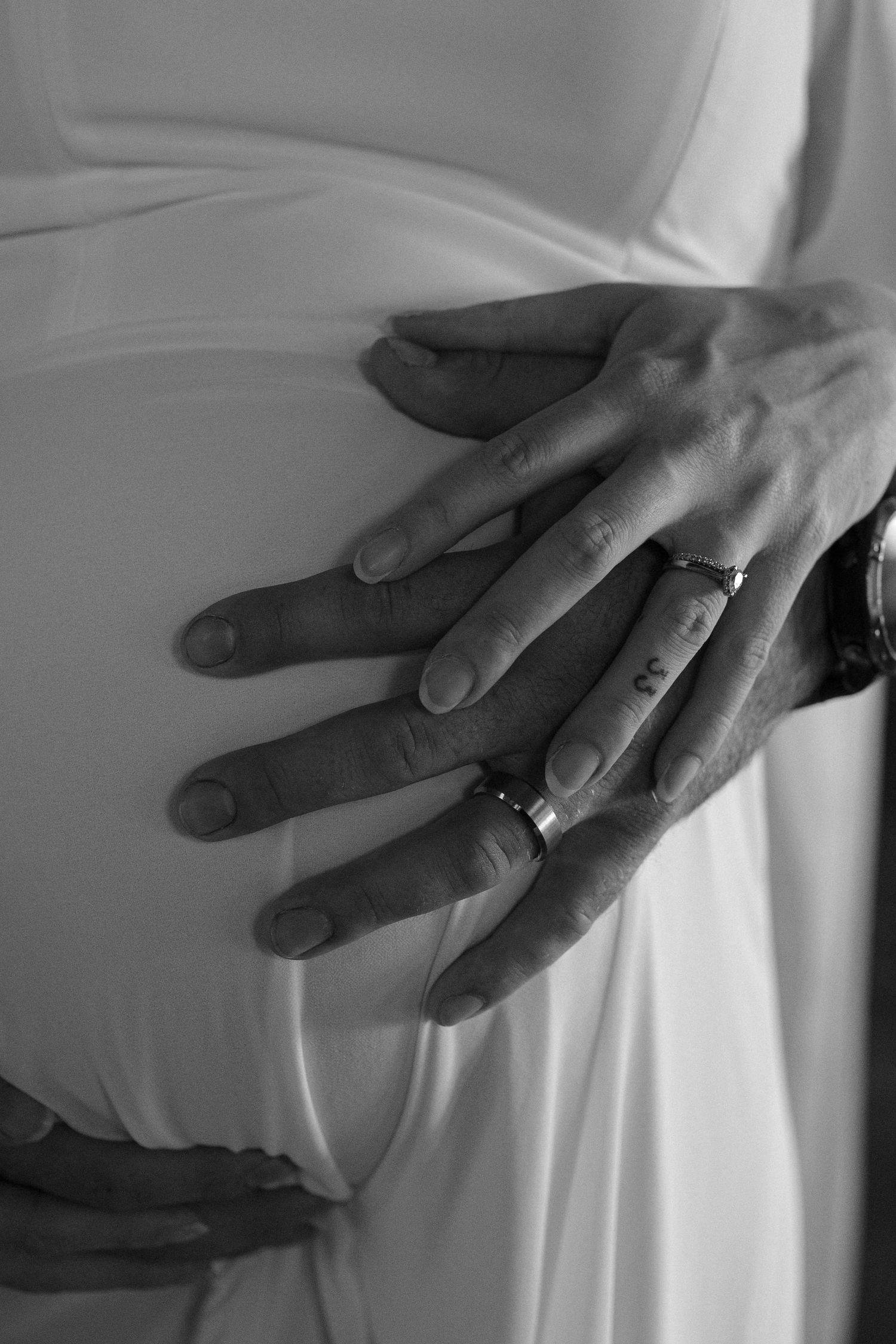 Black and white image of pregnant couples hands embracing her pregnant belly.