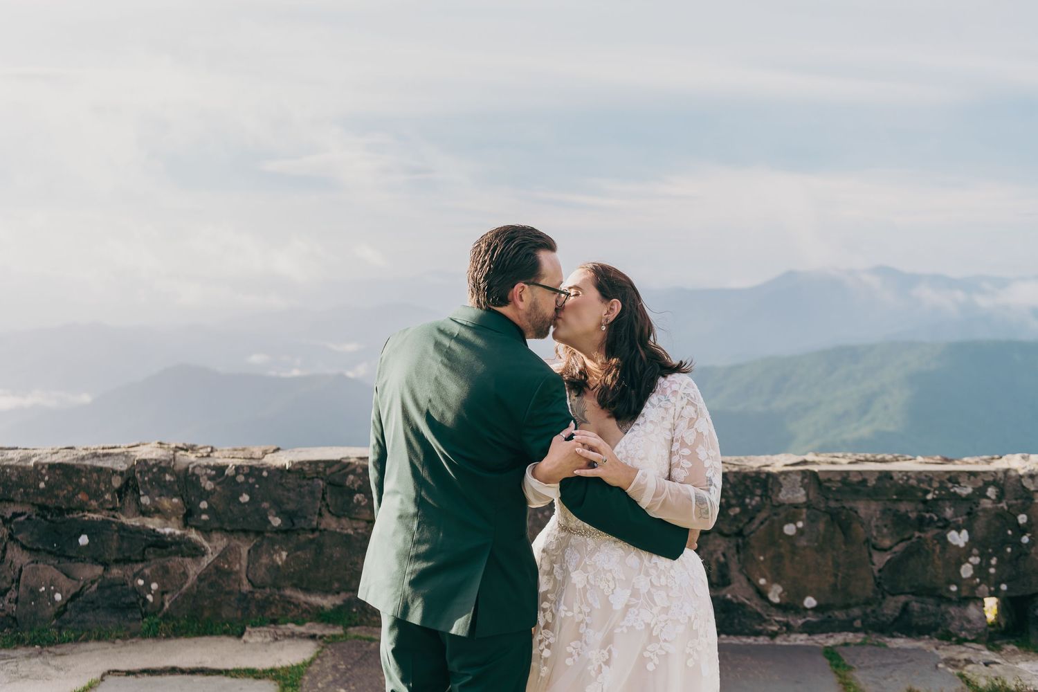 Couple shares a romantic kiss at an outdoor wedding venue with stunning mountain views in the background.