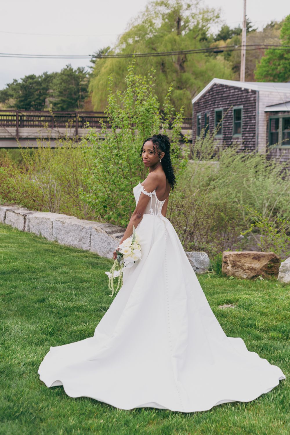 Bride in elegant off-shoulder white ball gown with long train posing in garden.