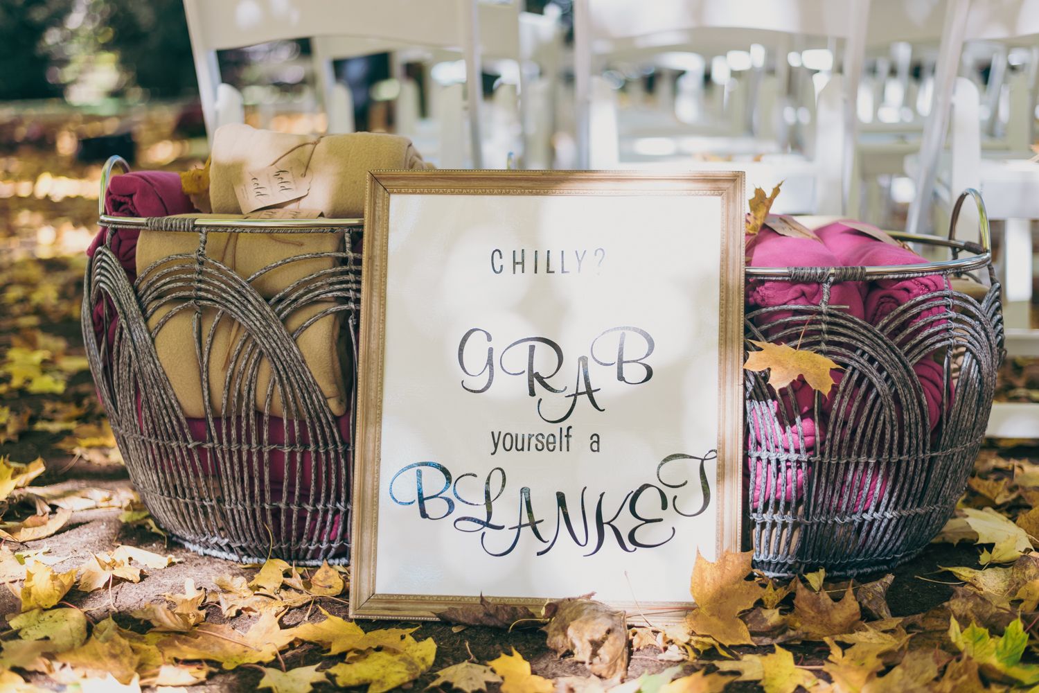 Wire baskets filled with pink blankets at an outdoor wedding with a sign reading Grab Yourself a Blanket.
