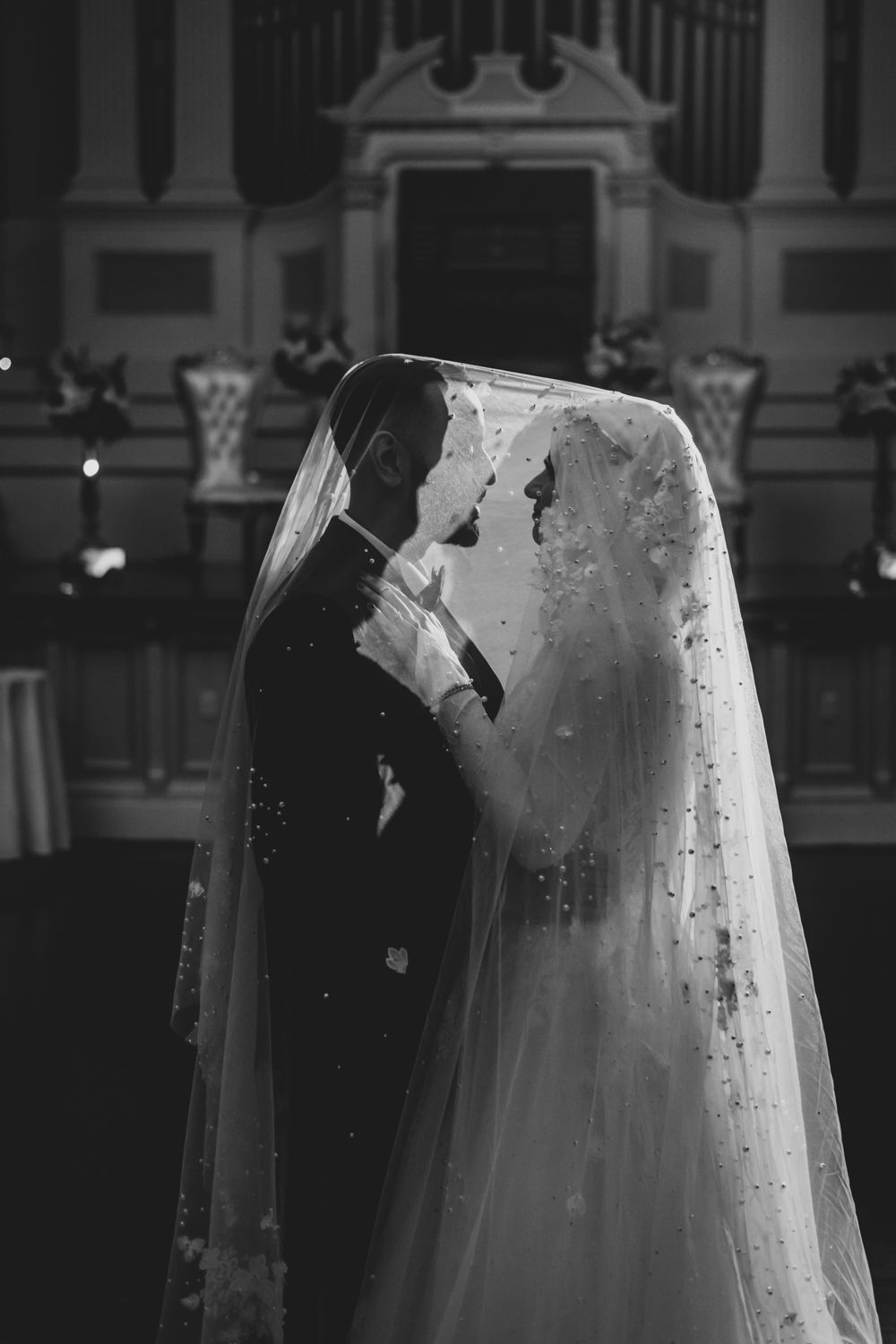 Elegant black and white photo of bride and groom under veil inside ornate church interior.