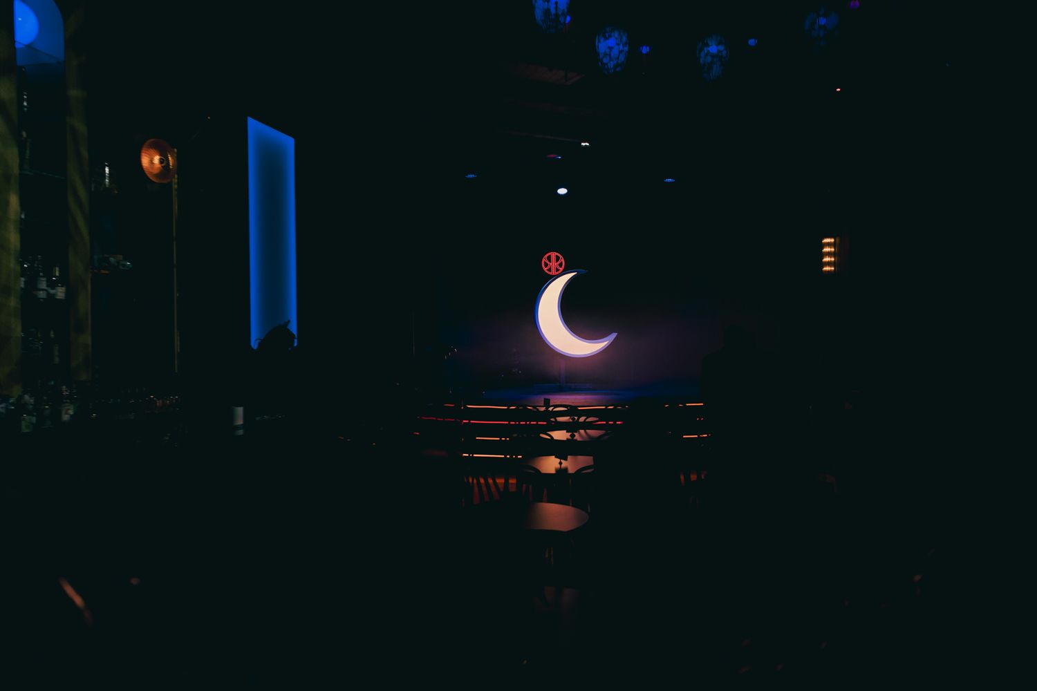 Glowing crescent moon decoration illuminates dark reception venue with moody blue ambient lighting.