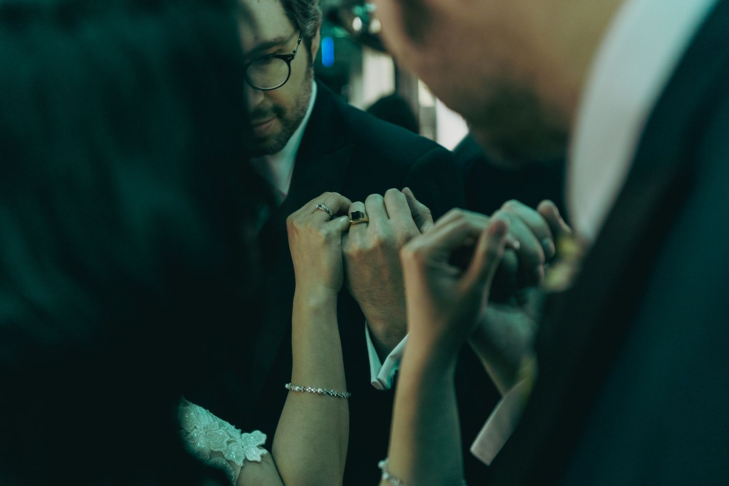 Close-up of hands exchanging wedding rings during an intimate ceremony in dimly lit surroundings.