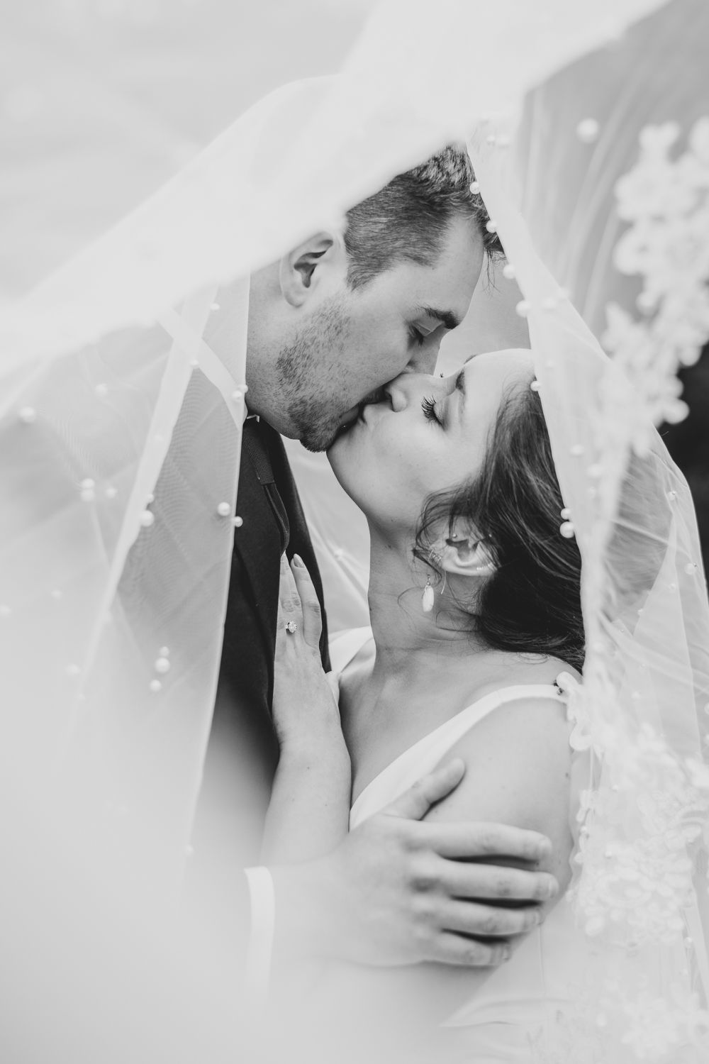 Black and white wedding photo of bride and groom kissing under a pearl-adorned veil.