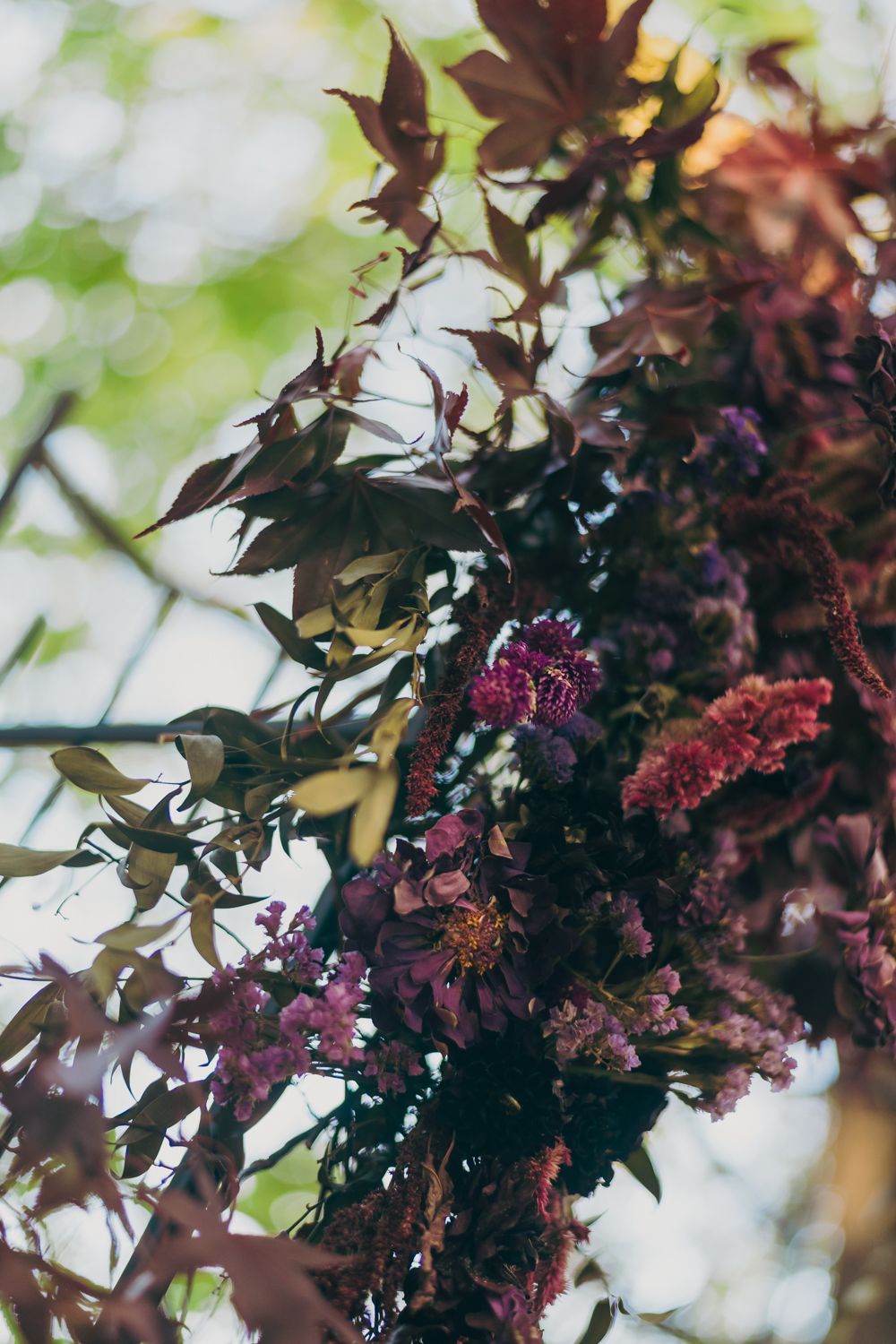 Lush floral arch adorned with deep purple and burgundy blooms and rich autumn foliage for a wedding ceremony.