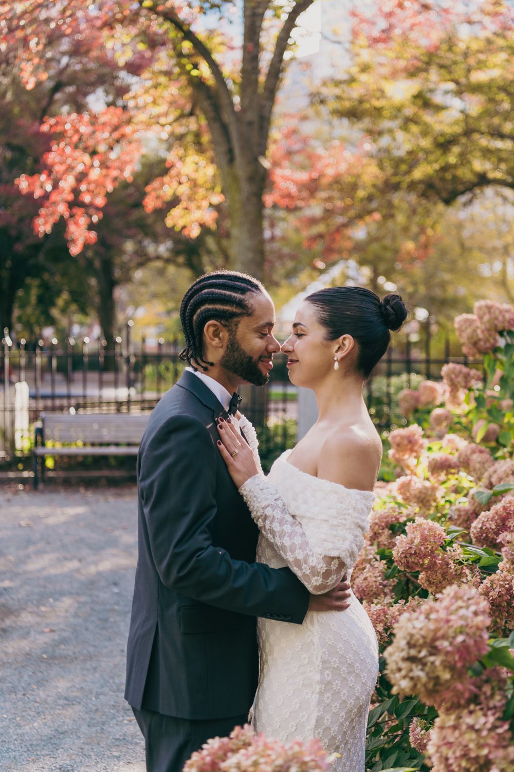 Couple in wedding attire sharing a romantic moment in an autumn park surrounded by hydrangeas and colorful foliage.