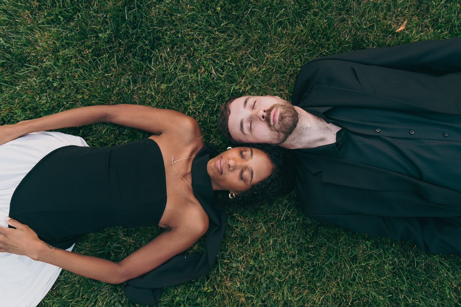 Couple lying on green grass together, smiling with eyes closed in a peaceful moment.