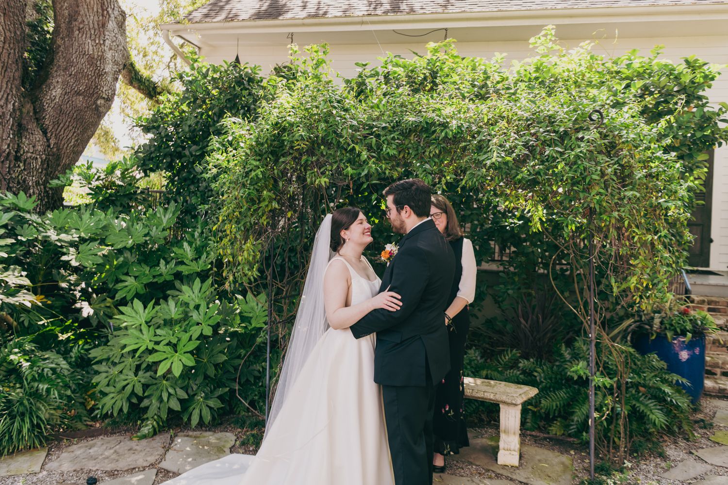 Bride and groom share a romantic moment beneath a lush green archway after their wedding ceremony.
