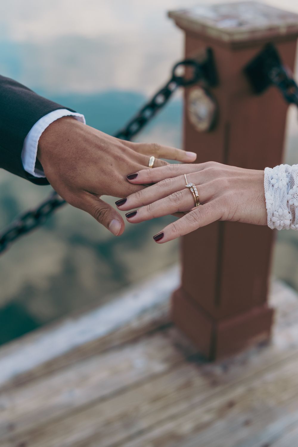 Close-up of newlywed couple's hands displaying matching gold wedding bands near a decorative chain post.