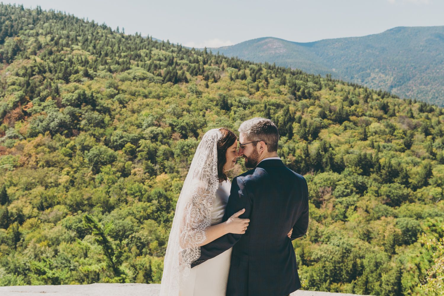 Romantic newlyweds embrace and kiss on a scenic mountain overlook.