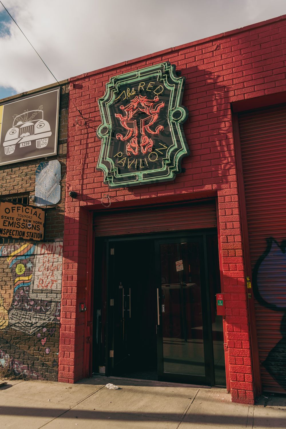 Red brick building exterior featuring a decorative neon sign for Tres Pavilion with graffiti-covered walls.