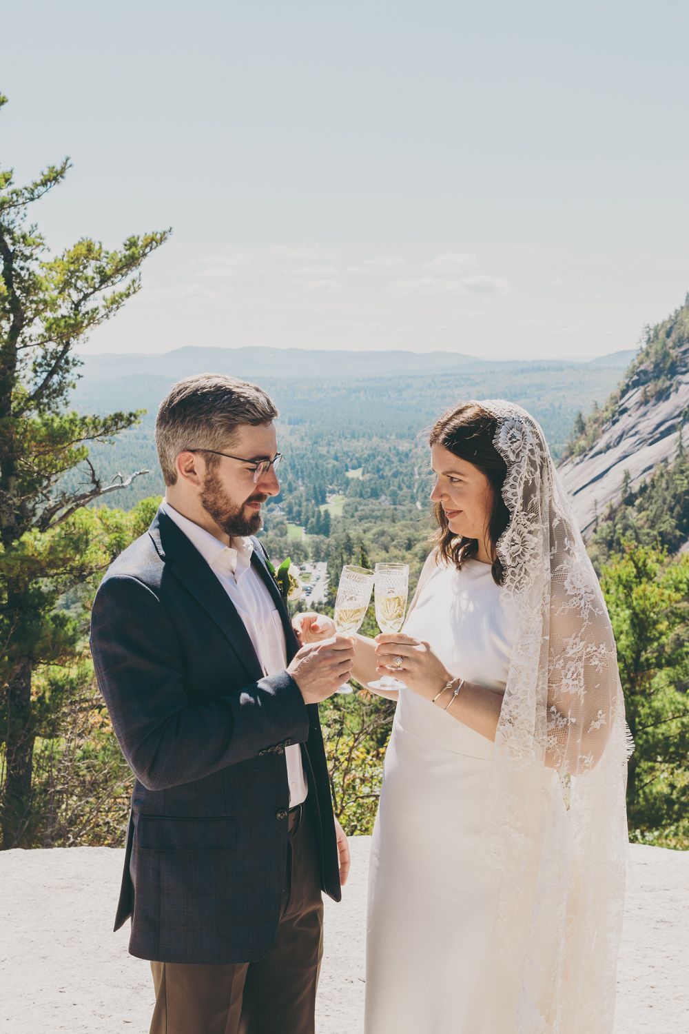 Happy couple shares champagne toast with breathtaking valley view behind them.