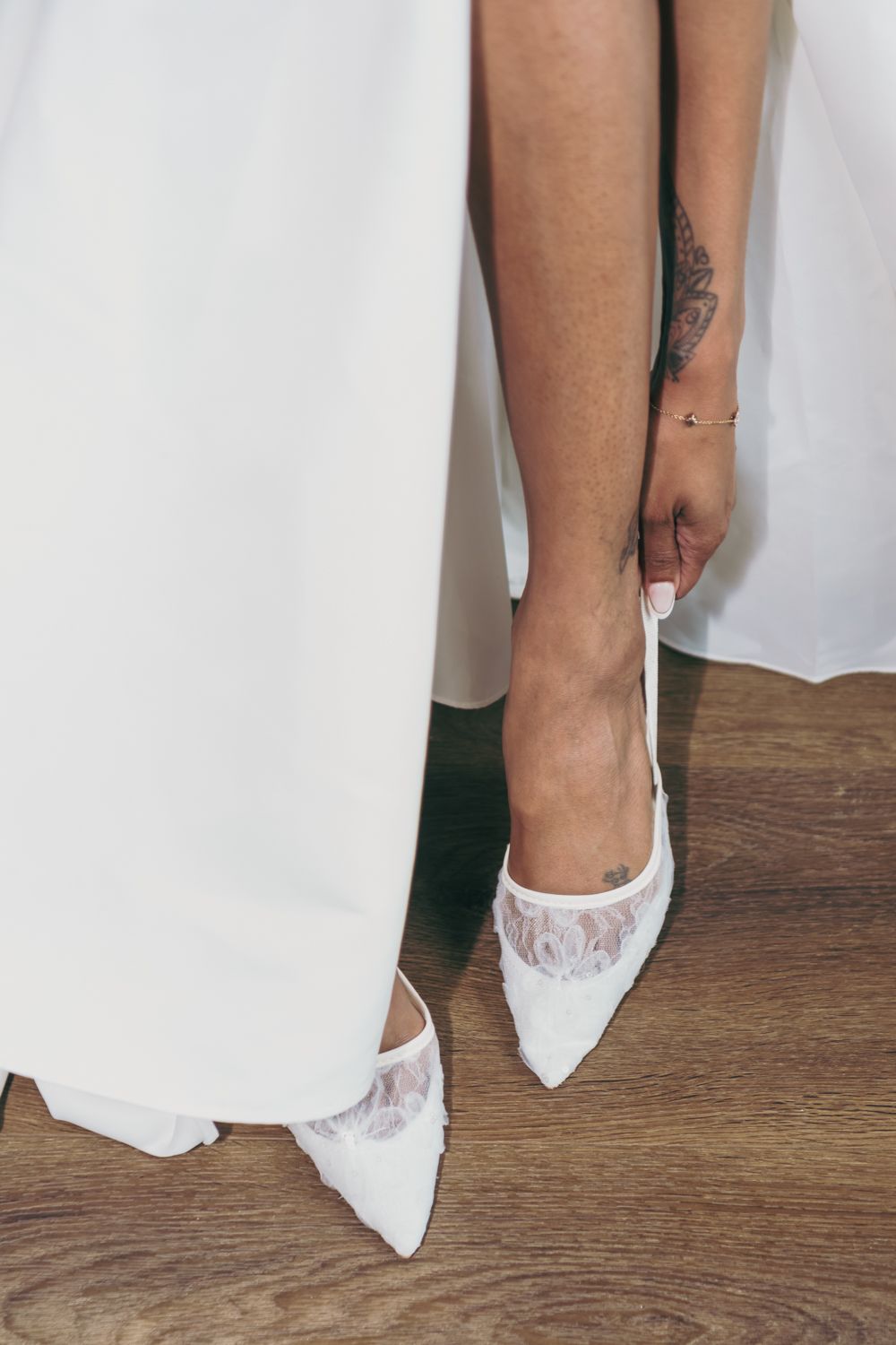 Bride wearing white lace pointed-toe wedding heels with a tattoo visible on her ankle.