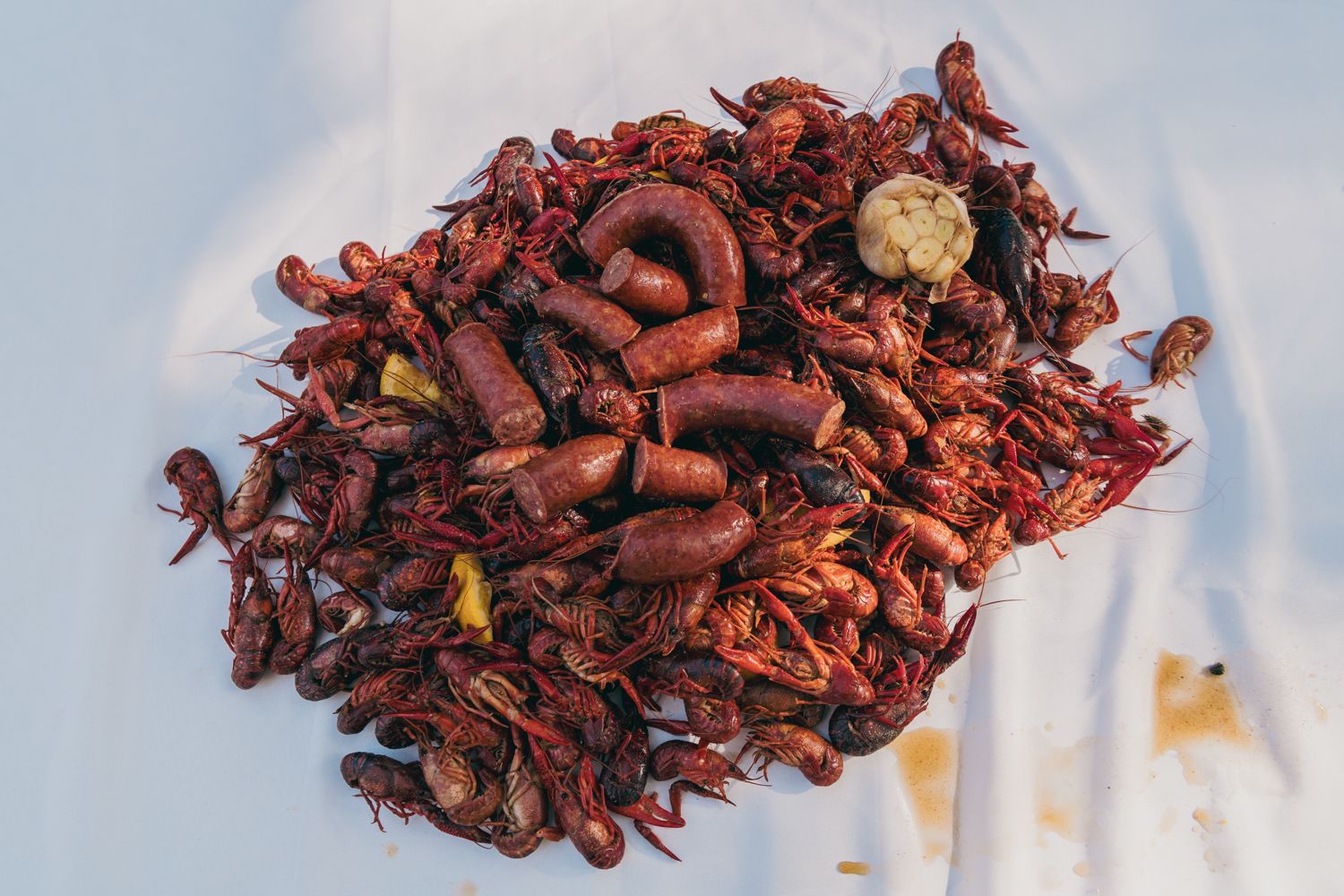 Pile of seasoned Cajun boiled crawfish and sausage served on white paper at an outdoor gathering.