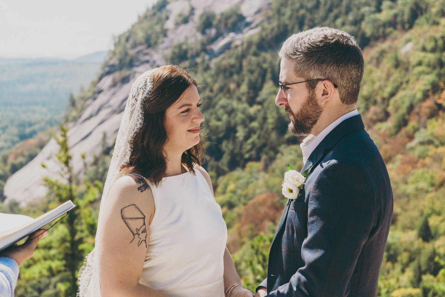 Bride and groom exchange vows outdoors with stunning mountain scenery behind them.
