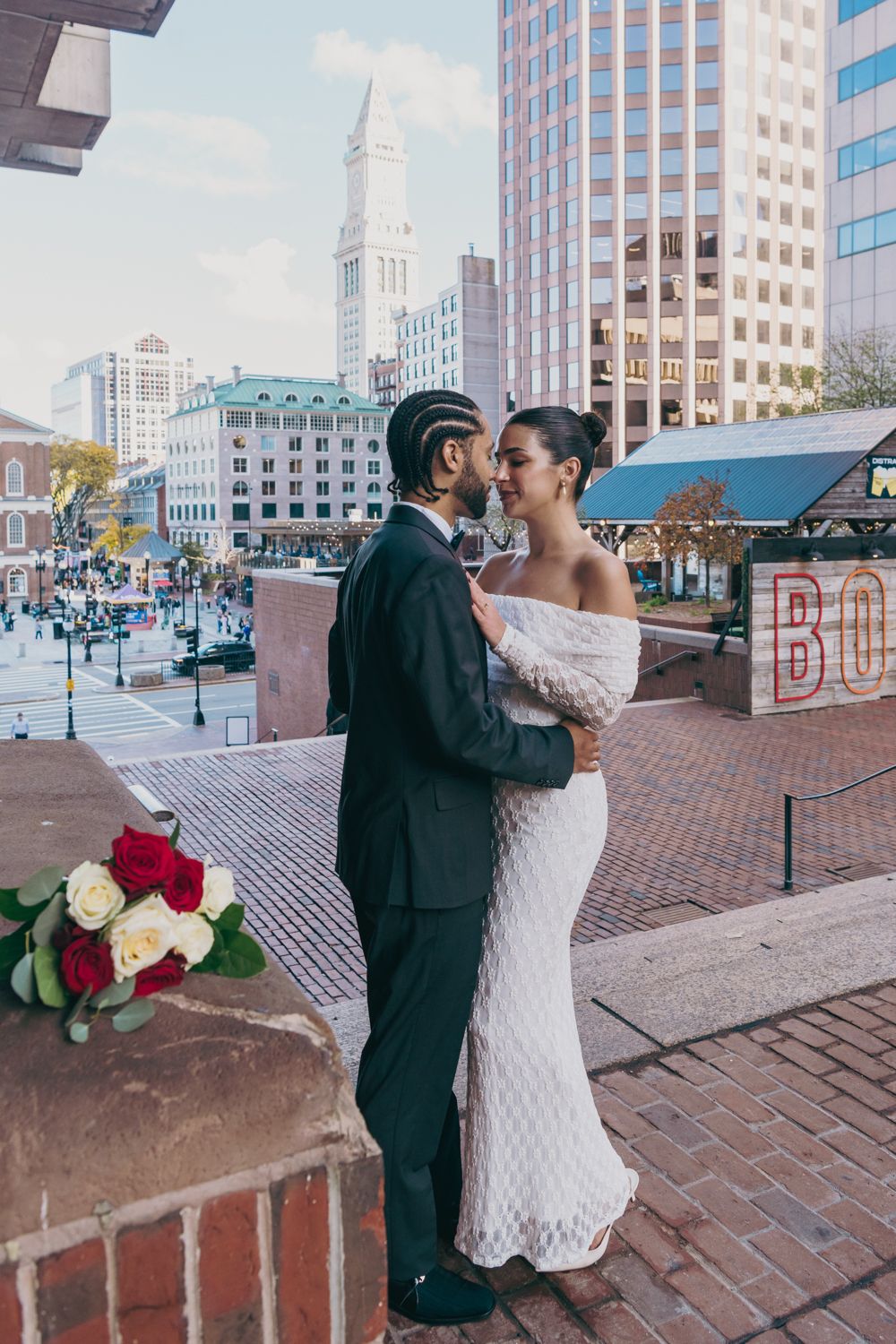 Bride and groom share a romantic kiss on a rooftop terrace with Boston city skyline and Custom House Tower in the background.