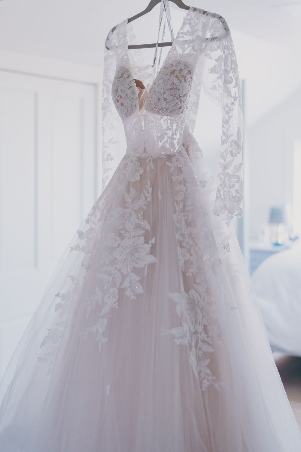 Elegant lace wedding gown with long sleeves and floral appliques hanging on a hanger.