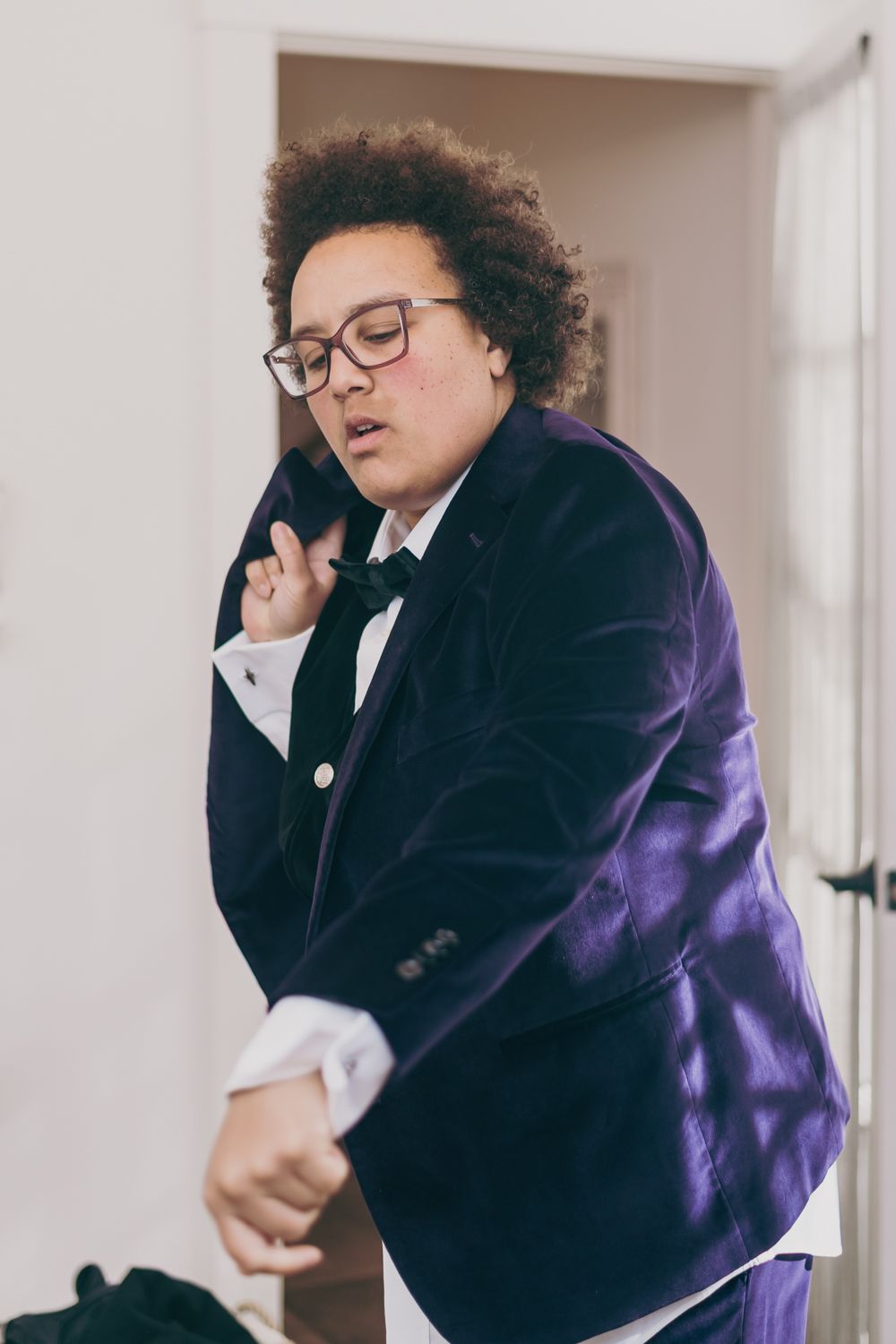 Young man in purple velvet tuxedo jacket and bow tie getting dressed for a formal event.