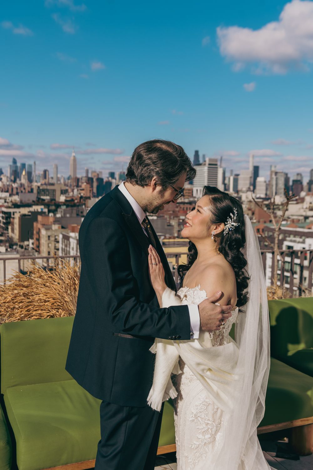 Bride and groom share romantic moment on rooftop with NYC skyline backdrop on sunny wedding day.