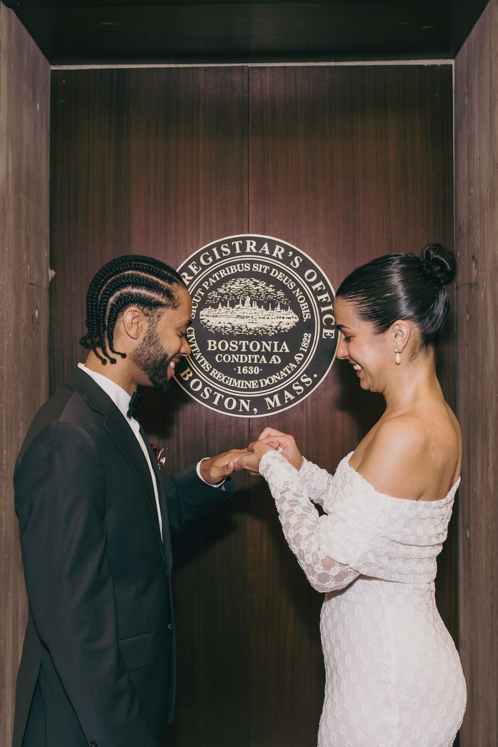 Bride and groom holding hands and smiling at Boston City Hall Registrar's Office during their wedding ceremony.