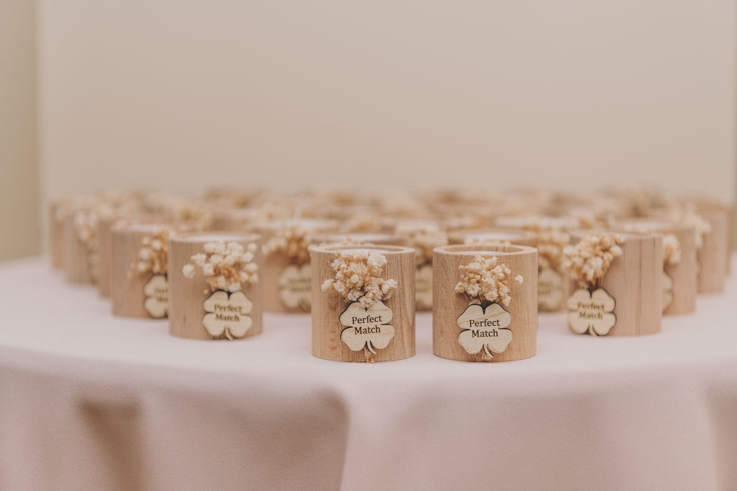 Elegant wedding favor candles decorated with dried flowers and name tags arranged on a pink tablecloth.
