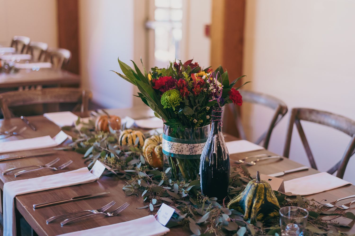 Rustic fall wedding reception table with floral centerpiece, gourds, greenery runner, and place settings.