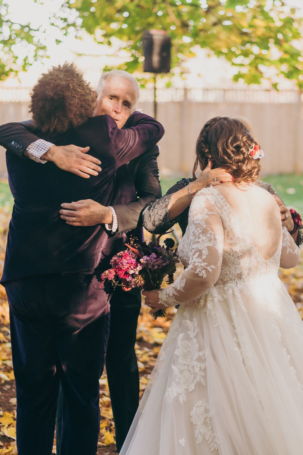 Newlyweds embracing guests with hugs after outdoor autumn wedding ceremony.