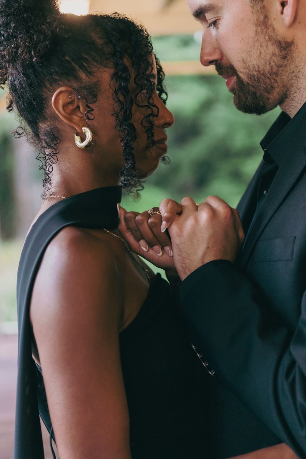 Close-up of interracial couple holding hands intimately, woman wearing gold hoop earrings and black dress.