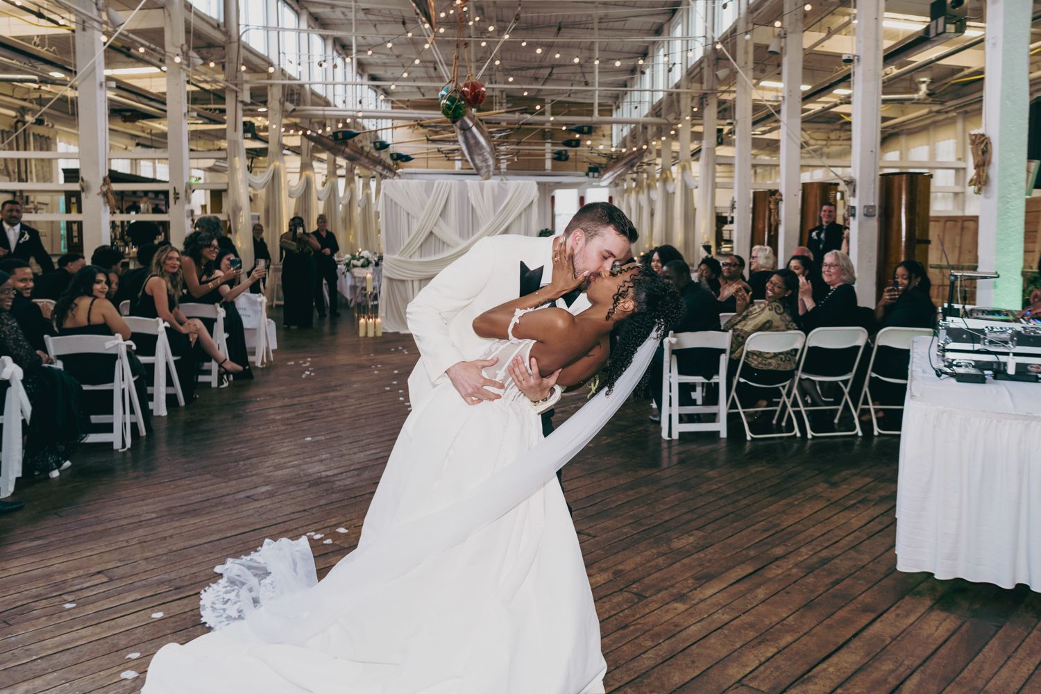 Groom dipping bride during first dance at indoor wedding reception venue.