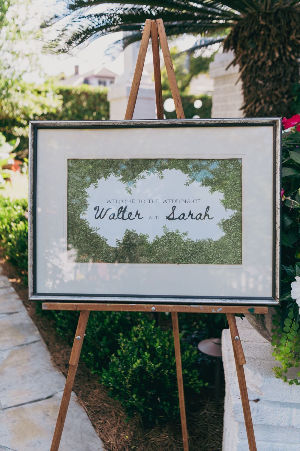 Elegant framed wedding welcome sign for Walter and Sarah displayed on a wooden easel outdoors.