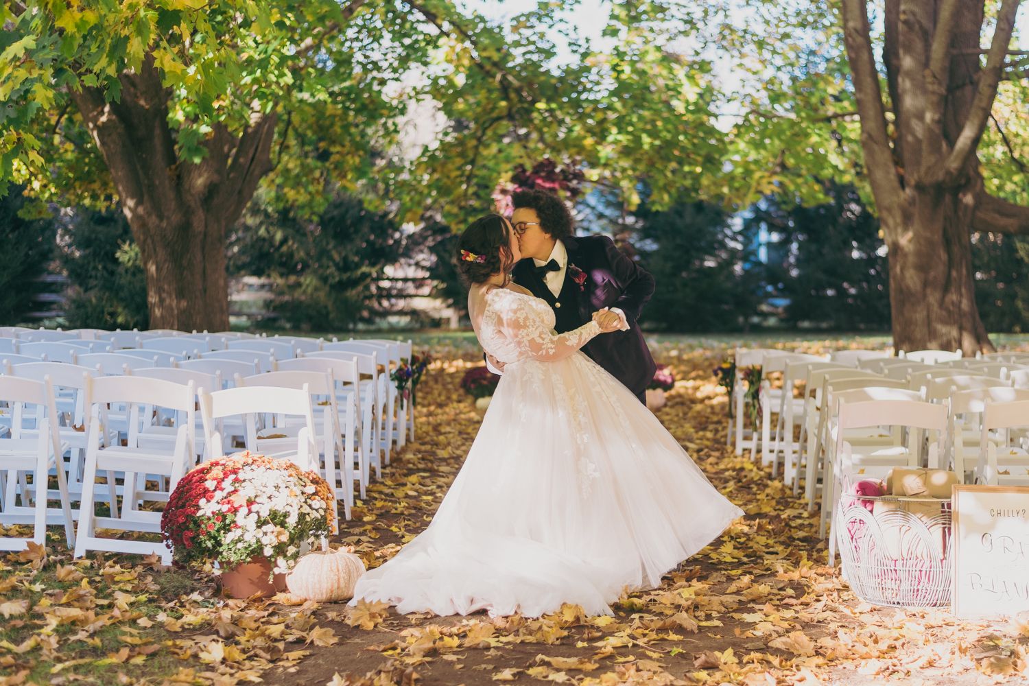 Bride and groom sharing romantic dip kiss at outdoor fall wedding ceremony aisle.